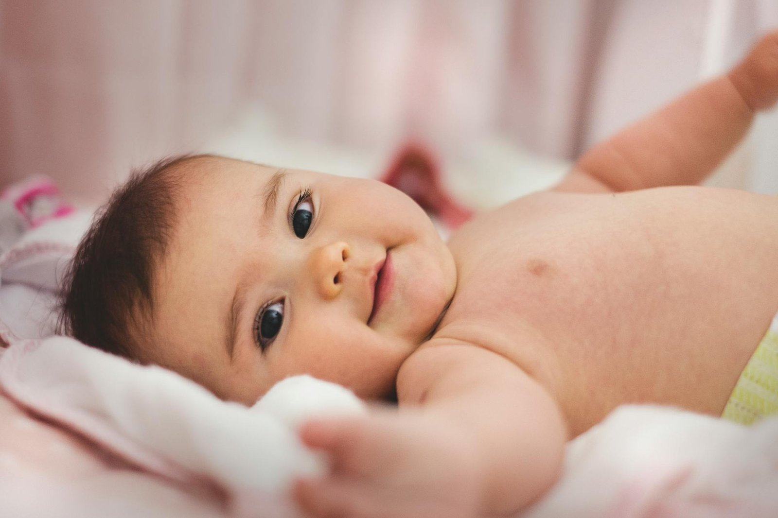 Cute baby lying on a soft bed, expressing innocence and joy in a cozy indoor setting.